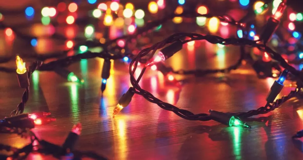 The image shows a string of colorful Christmas lights, illuminated in red, green, blue, and yellow, tangled together and placed on a wooden surface.
