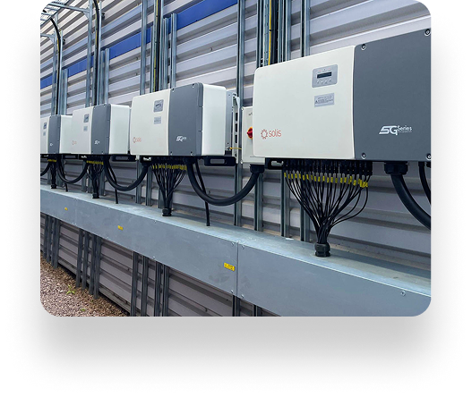 Five Linney solar inverters mounted in a row on a metal rack, with wires extending from each unit, against a corrugated metal wall in an industrial setting.