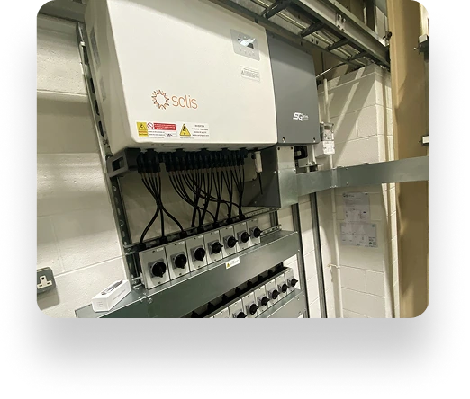 Solis solar inverter and electrical panel on a wall, installed by Mintdale Engineering. Cables connect below, with conduits and a small router on the left. Indoor control area setup.