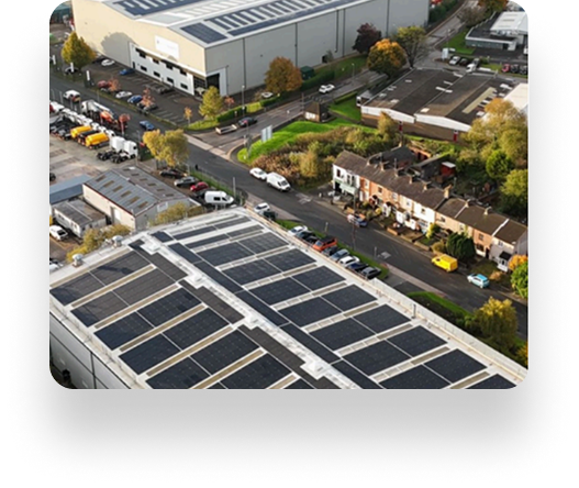 Aerial view of an industrial area with solar-paneled buildings and Pyroguard windows, next to a road dividing them from houses and cars, surrounded by autumn trees.