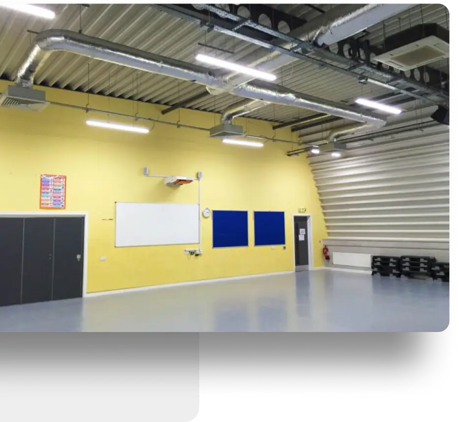 Yellow-walled room with whiteboard, posters, exposed pipes, and smooth gray flooring.