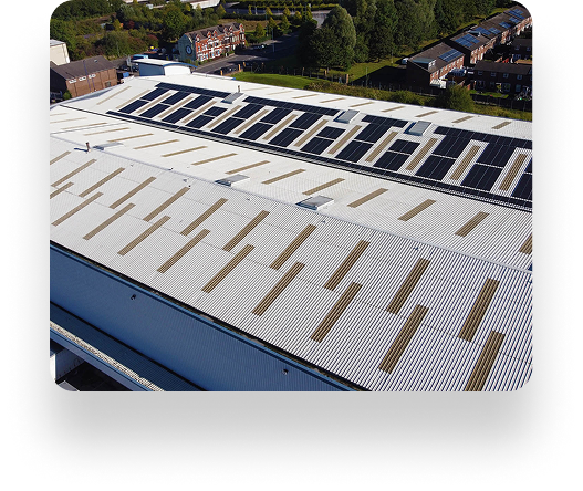 Aerial view of Searchlight Electrics large industrial building with solar panels on the white roof, surrounded by greenery and residential houses.