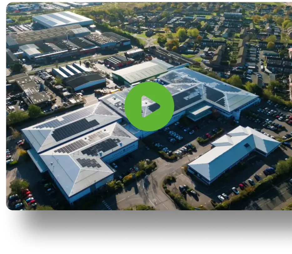 Aerial view of industrial buildings with solar panel rooftops, cars, and greenery.