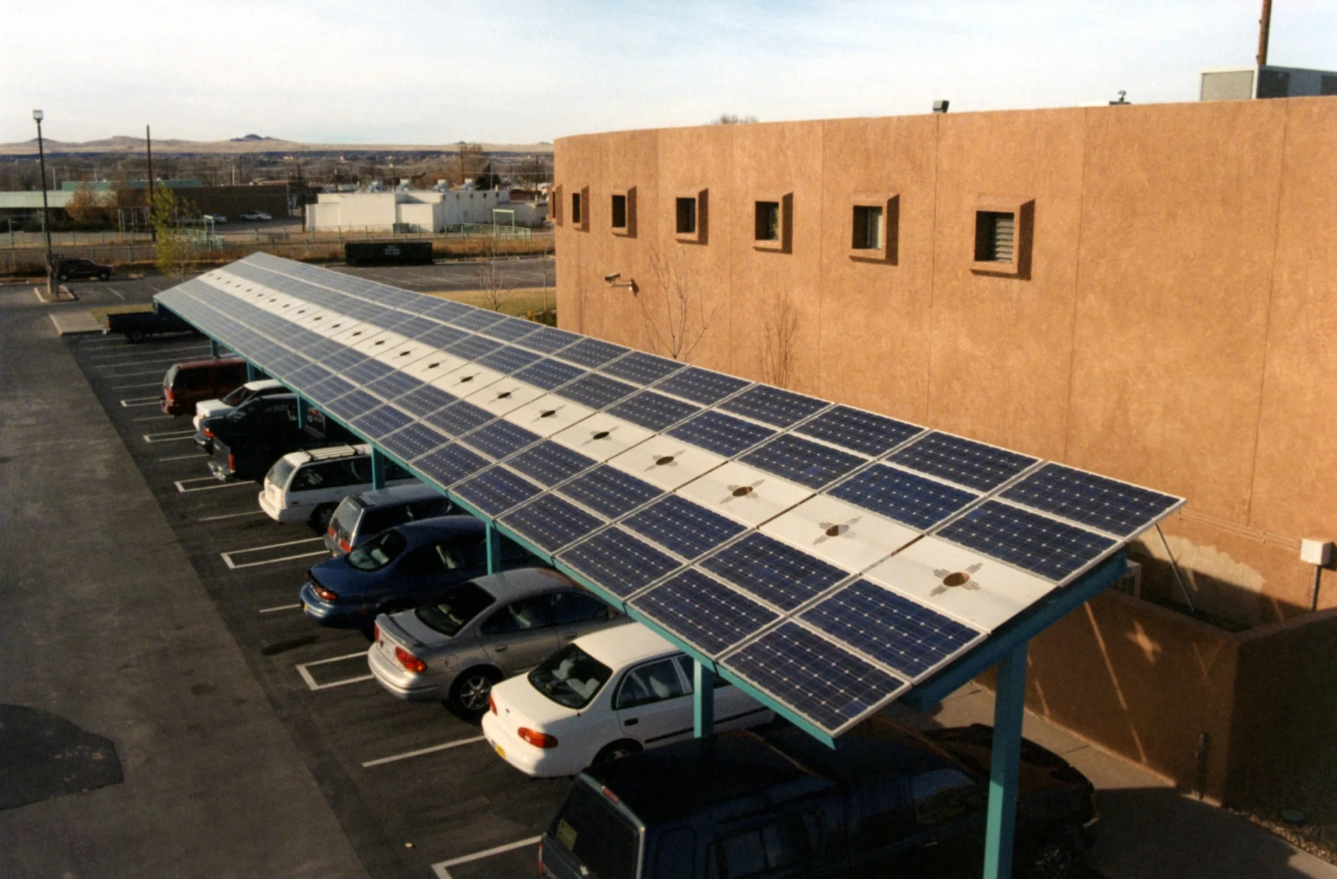 A parking lot featuring cars shaded by large solar panel structures in a sunny setting.
