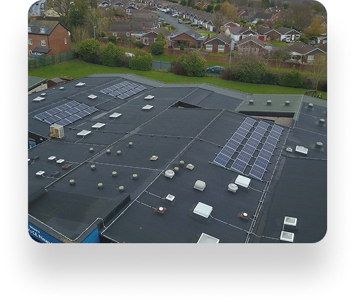 Aerial view of a building with solar panels on its flat roof, situated near St Andrews Primary School among houses, trees, and greenery.