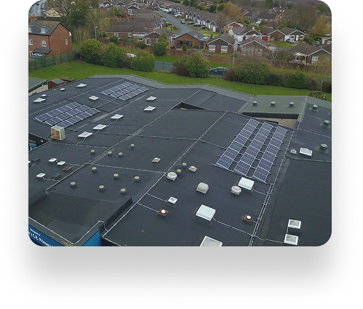 Aerial view of a building with solar panels on its flat roof, situated near St Andrews Primary School among houses, trees, and greenery.