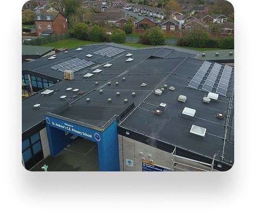 Aerial view of St Andrews Primary School with solar panels and ventilation units on the roof, surrounded by residential homes and lush greenery.