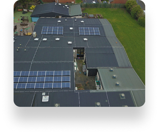 Aerial view of St Andrews Primary School, featuring solar panels on the roof. The building is surrounded by grass, with skylights and vents alongside the panels.