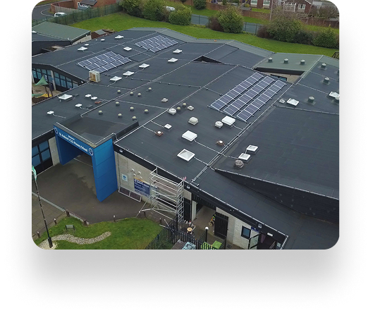 Aerial view of St Andrews Primary School with solar panels on the roof, a blue entrance sign, grassy areas, and surrounding trees.