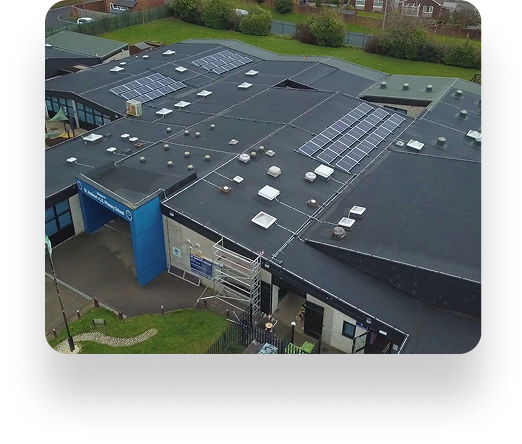 Aerial view of St Andrews Primary School with solar panels on the roof, a blue entrance sign, grassy areas, and surrounding trees.