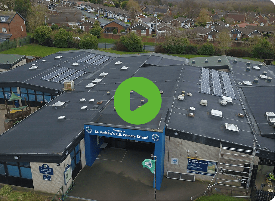 Aerial view of St Andrews Primary School with solar panels on the roof. The entrance sign confirms its St. Andrews C.E. Primary School, surrounded by a neighborhood. A green play button graphic invites exploration.