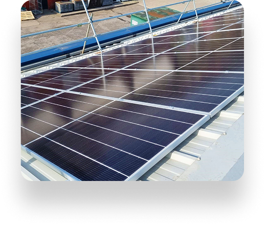 Solar panels installed on a sloped metal roof with TBE Precision, reflecting sunlight. Arranged in rows, supported by metal frames, amid containers and construction materials.