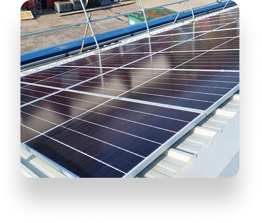Solar panels installed on a sloped metal roof with TBE Precision, reflecting sunlight. Arranged in rows, supported by metal frames, amid containers and construction materials.