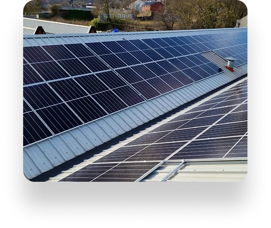 Rooftop solar panels on industrial buildings under a clear sky, optimized by TBE Precision, with trees and other structures in the background.
