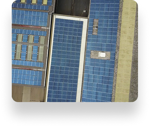 Aerial view of The Box Factorys rooftops covered with various sizes of blue solar panels, surrounded by a stone pathway and nearby buildings, merging technology with industry.