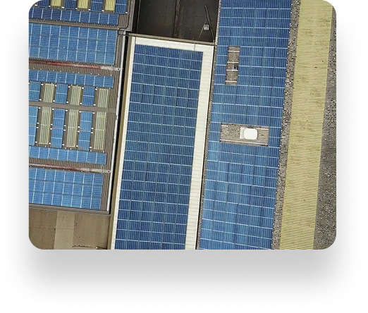 Aerial view of The Box Factorys rooftops covered with various sizes of blue solar panels, surrounded by a stone pathway and nearby buildings, merging technology with industry.
