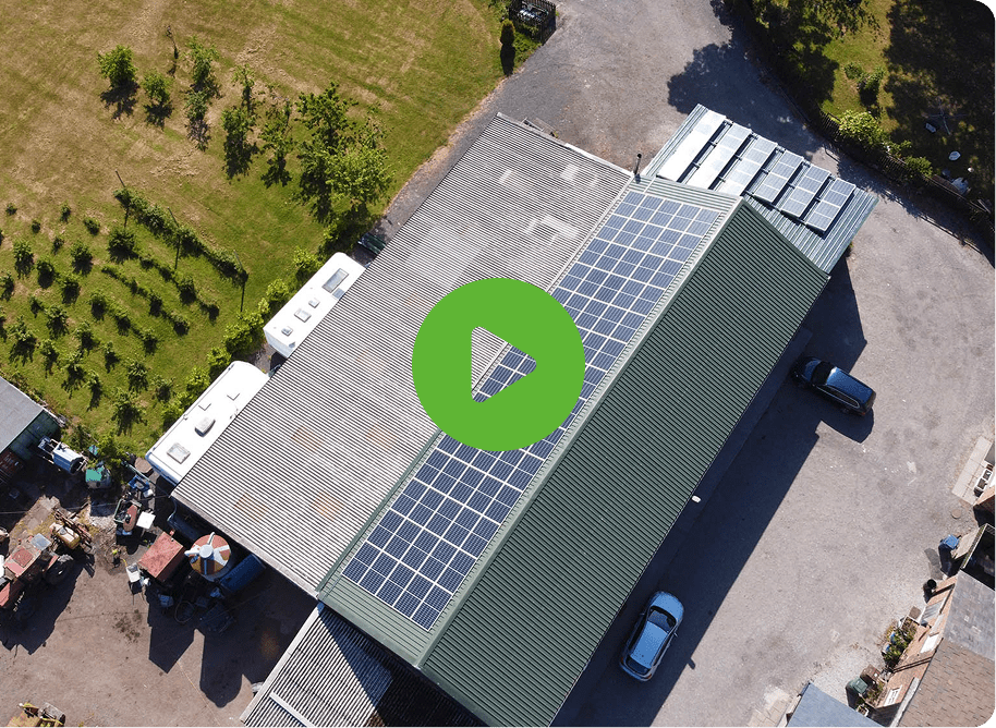 Aerial view of The Farm Burscough shows a large building with solar panels and a green roof, surrounded by grass and parked vehicles. A play button icon overlays the image.