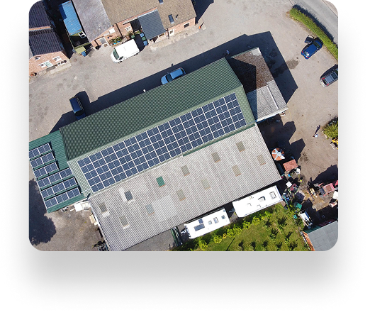 Aerial view of The Farm Burscoughs industrial buildings with solar panels, cars parked nearby, and various items scattered. Surrounding area features a mix of paved and unpaved surfaces.