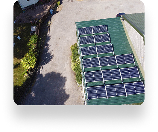 Aerial view of solar panels on a green rooftop at The Farm Burscough. Nearby, a gravel area with trees and a fence casts gentle shadows on the ground.