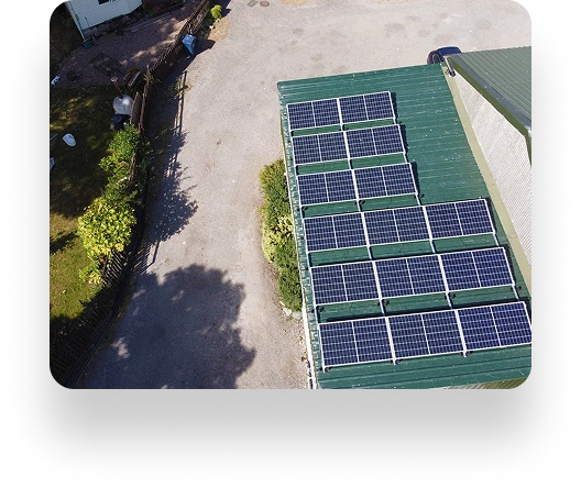 Aerial view of solar panels on a green rooftop at The Farm Burscough. Nearby, a gravel area with trees and a fence casts gentle shadows on the ground.