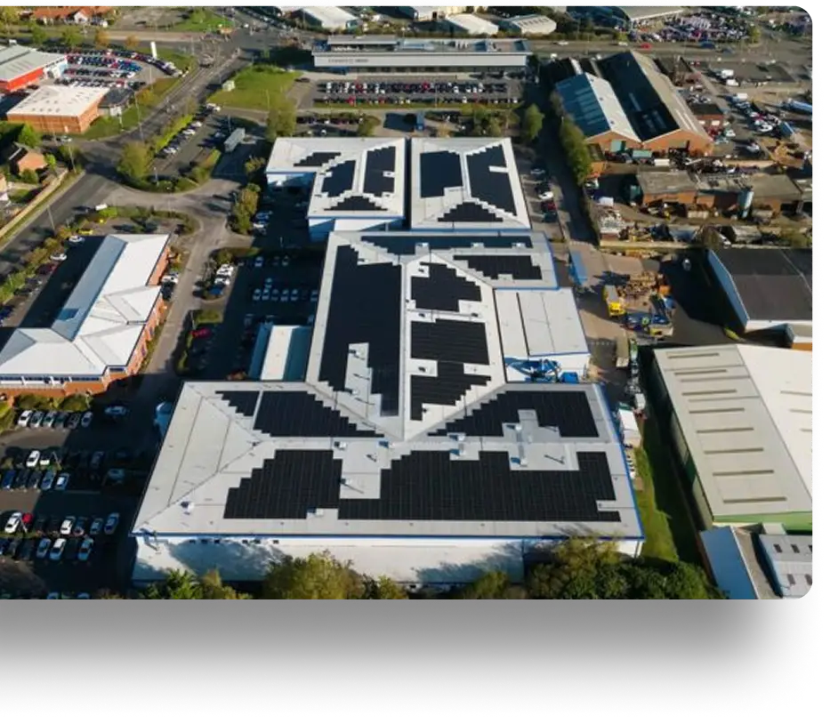 Aerial view of a large building with creatively arranged solar panels on the roof, forming the image of a bird. The surrounding area includes parking lots, roads, and other industrial buildings.