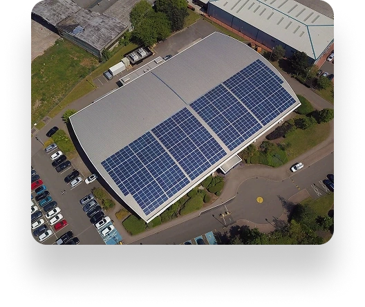 Aerial view of a UBT facility with a solar-paneled rooftop, surrounded by a parking lot, green spaces, nearby buildings, and trees.