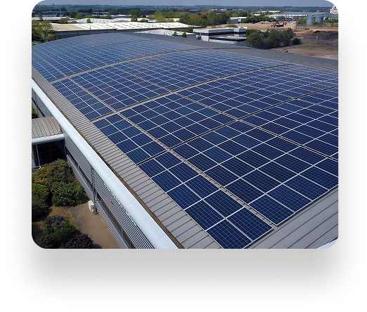A large industrial building with a rooftop fully covered in UBT solar panels. Trees and industrial structures are visible in the background.