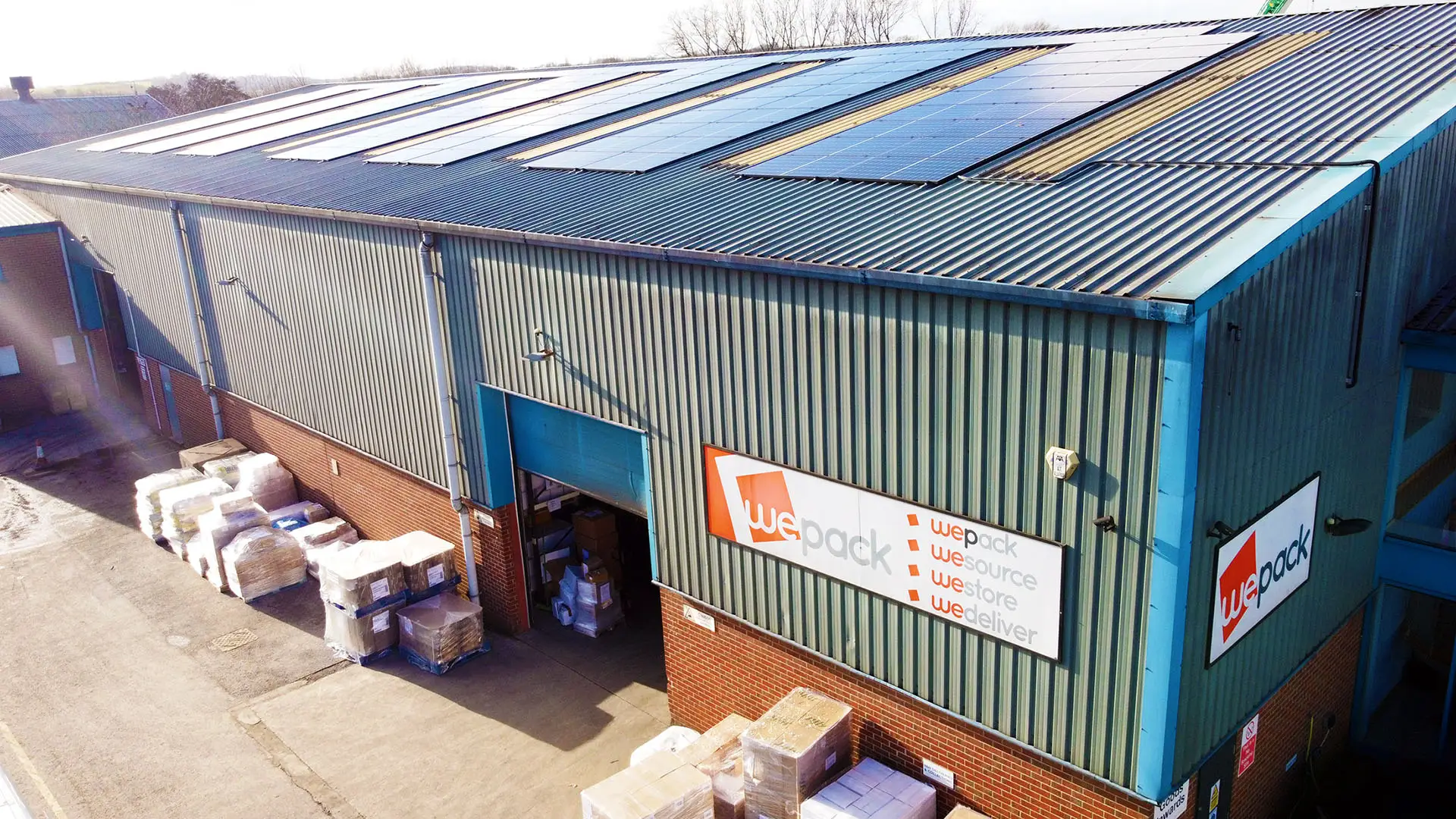 Large warehouse with solar panels, goods stacks, and 'WePack' signage.