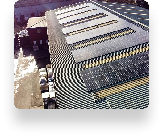 Rooftop view of WePack facility with solar panels on corrugated metal roof, surrounded by industrial materials. Adjacent warehouse buildings visible in the background.