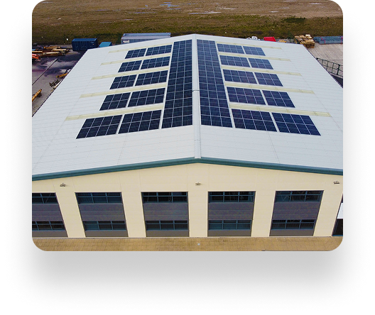 Aerial view of a Wefen industrial building with solar panels on its white roof, surrounded by open land. The eco-friendly structure has multiple windows on each side.
