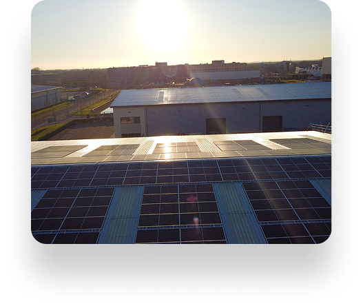 Sunset over Wefens rooftop solar panels in an industrial area; a building and skyline form a dramatic backdrop.