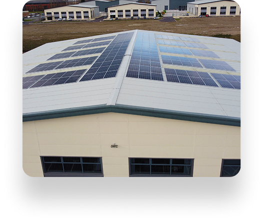 A large industrial building with Wefen solar panels on its roof; similar buildings in the background under a clear, sunny sky.