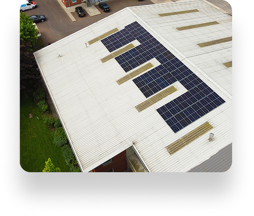 Aerial view of Westbrook Industrials large white building with solar panels on the roof, surrounded by green grass and a few parked cars.