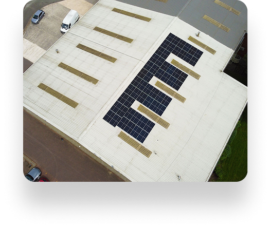 Aerial view of Westbrook Industrial rooftop: a neat rectangular array of solar panels is centered amidst skylights on a white roof. Nearby, a parking area holds several cars.