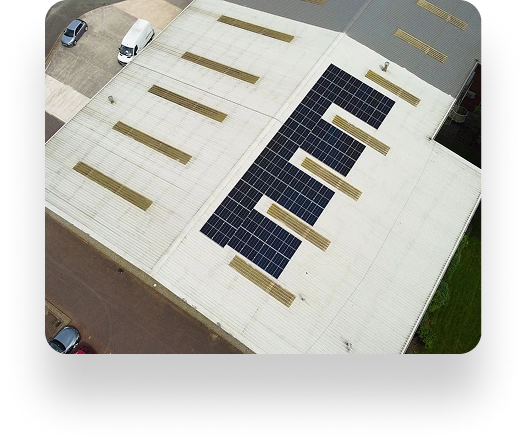 Aerial view of Westbrook Industrial rooftop: a neat rectangular array of solar panels is centered amidst skylights on a white roof. Nearby, a parking area holds several cars.