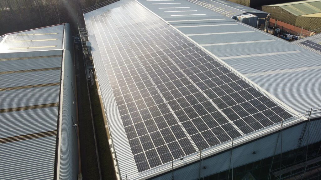 Aerial view of an industrial building with solar panels installed on the rooftop, surrounded by other structures.