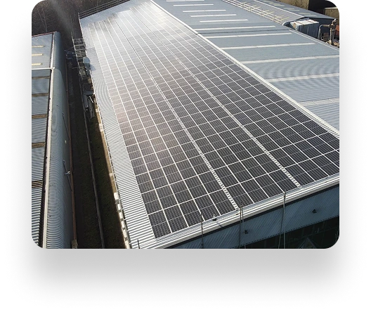 Rooftop view of a large industrial building with Datim solar panels. Panels are neatly arranged, capturing sunlight. Nearby are structures and vehicles, indicating an industrial setting.