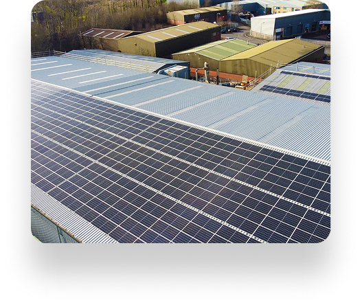 Aerial view of large industrial buildings with solar panels on roofs, surrounded by trees and structures under a clear sky, blending technology and nature.