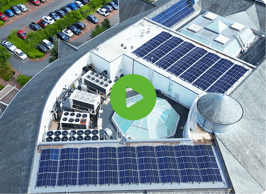 Aerial view of a rooftop with solar panels, ventilation units, and a glass dome. Zen Internet logos are visible, surrounded by parking lots and trees. A green play button overlays the image.