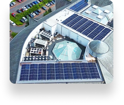 Aerial view: building roof with solar panels, showcasing modern efficiency like Zen Internet. Centered circular glass structure with HVAC units; cars parked in adjacent lot.