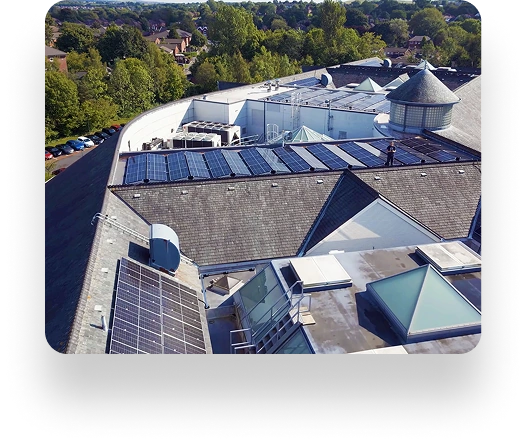 Aerial view of a rooftop with solar panels, highlighting Zen Internets sustainability. The building has flat and sloped surfaces with skylights, surrounded by greenery and a parking lot.