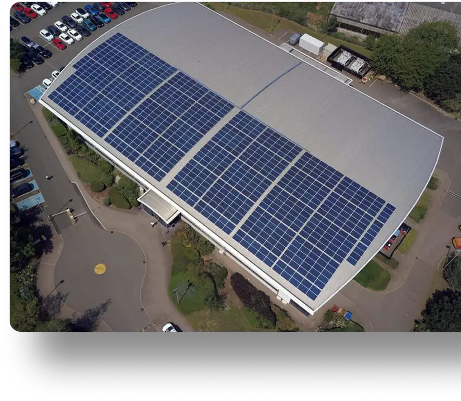 Aerial view of a solar-powered building surrounded by parking areas, cars, and lush greenery.