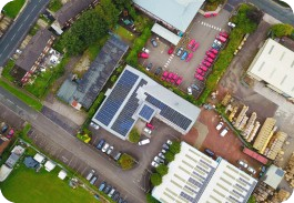 Aerial view of an industrial area with solar panels on a building roof, parking lots, and vehicles.