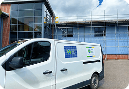 White van with a blue grid logo parked in front of a modern building with scaffolding and large windows.