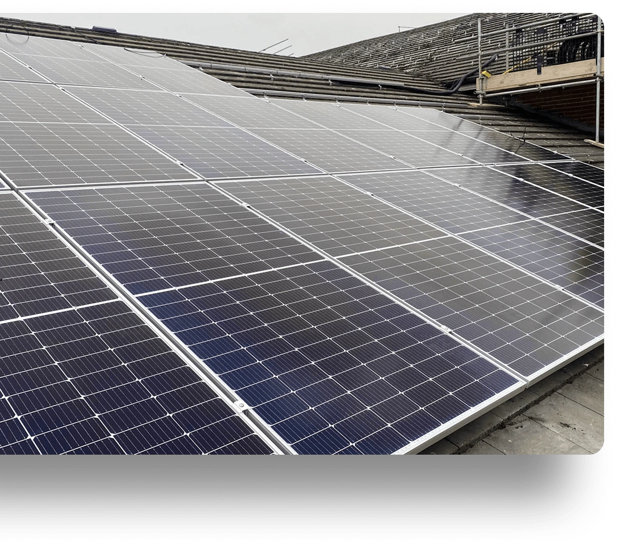Close-up of solar panels on a sloped rooftop, capturing overcast light. Panels are in neat rows, forming a geometric pattern. Background shows additional roof structures.