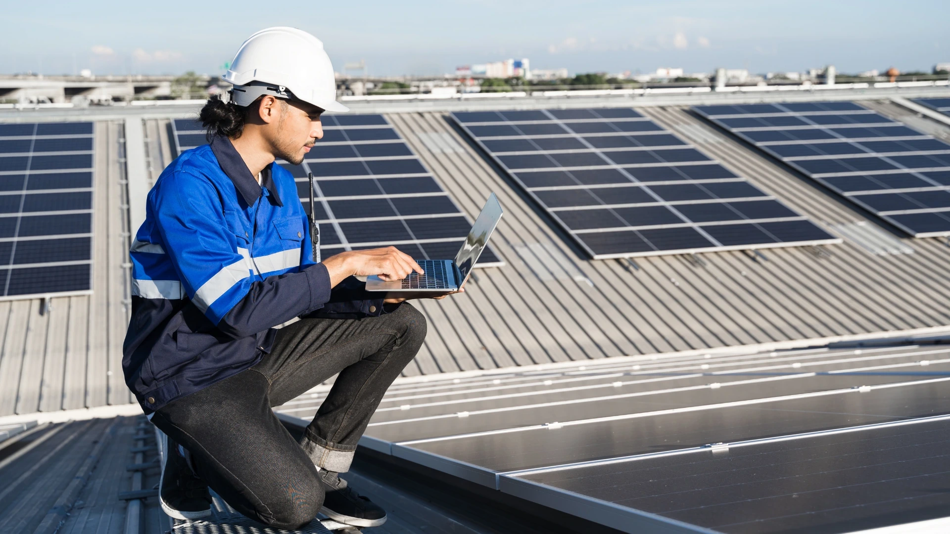 Technician using a laptop on a rooftop with solar panels.