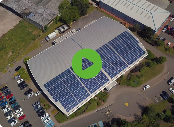 Aerial view of a commercial building with solar panels on its roof, surrounded by parked cars and industrial area.
